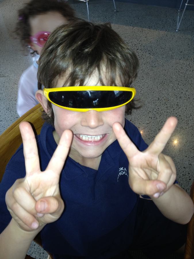 Boy wearing yellow visor sunglasses, making peace signs with both hands