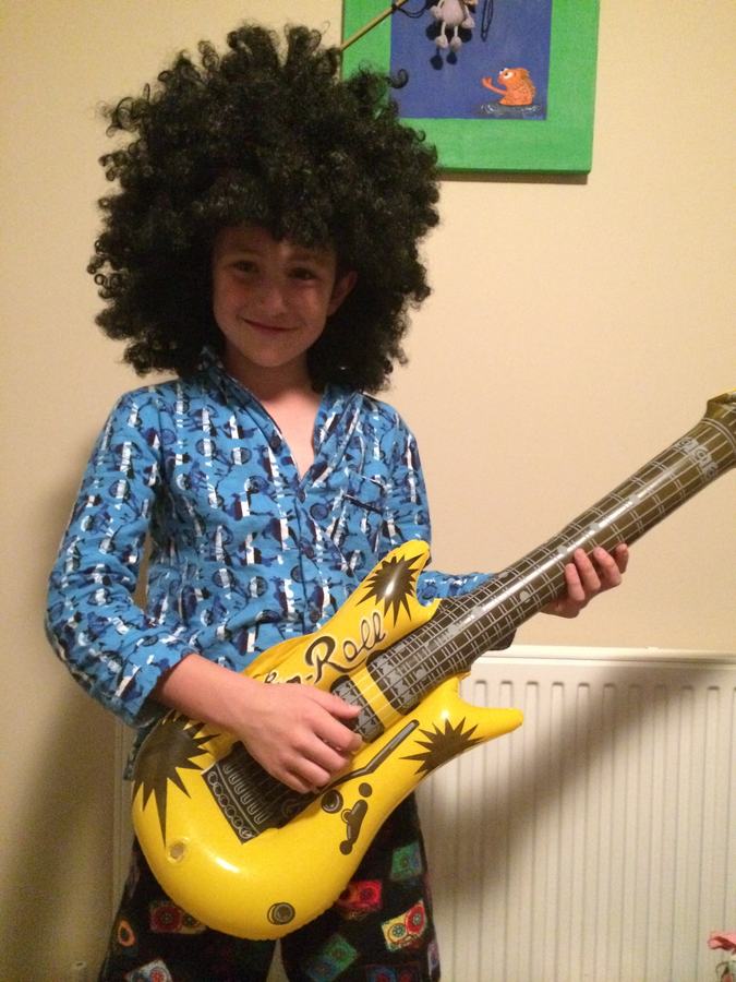 Boy in a curly wig playing an inflatable guitar
