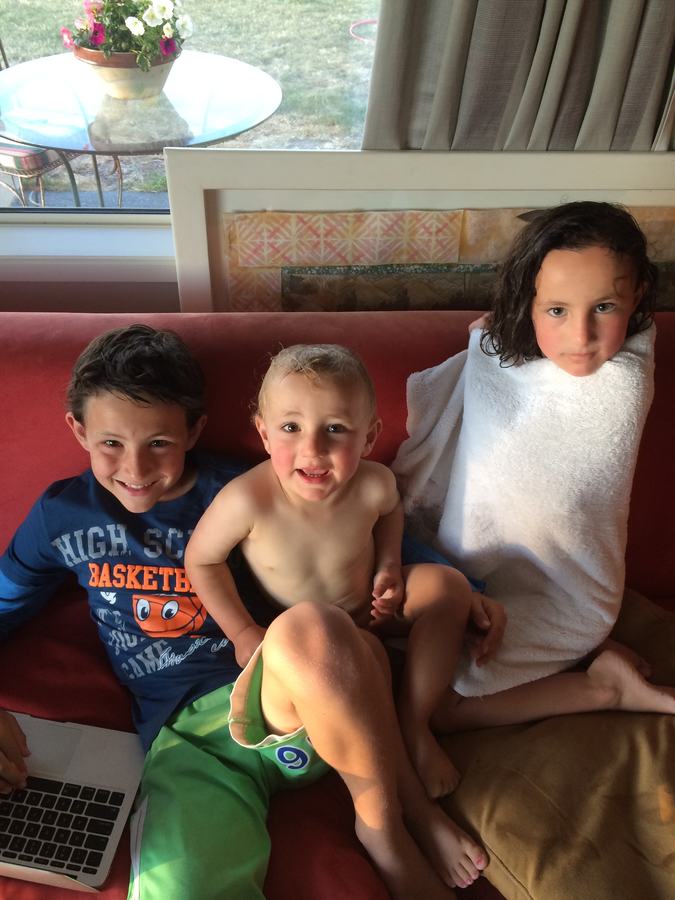 Three children wrapped in towels on a red sofa