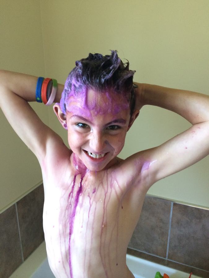 Boy covered in purple paint, arms raised in the bathroom