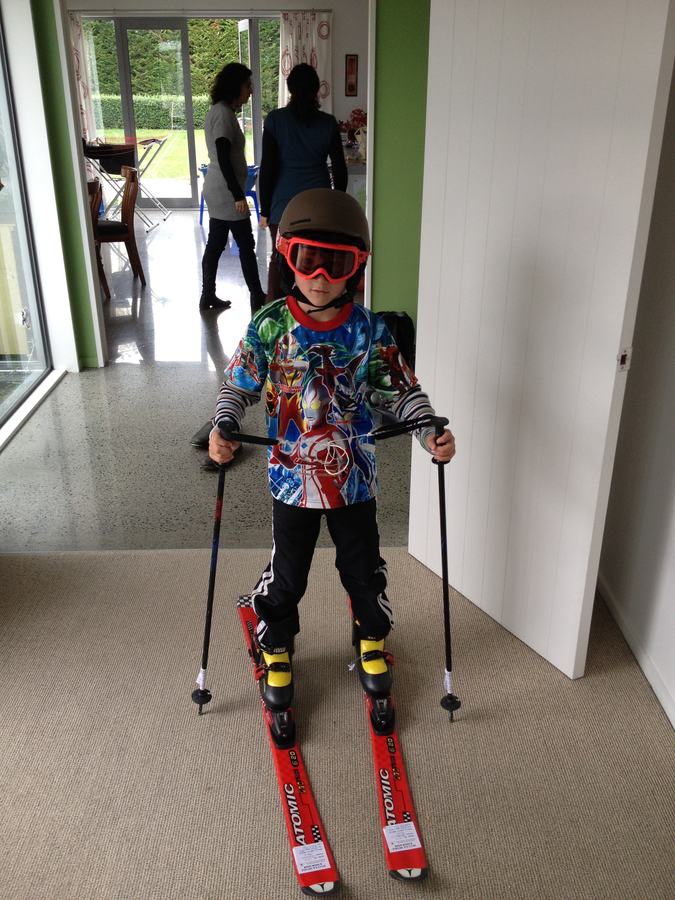 Boy dressed in full ski gear with helmet, goggles and poles at home