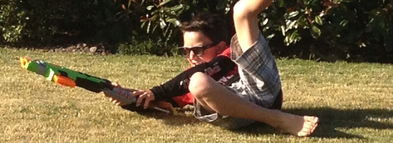 Boy in sunglasses sitting on the grass with a water blaster