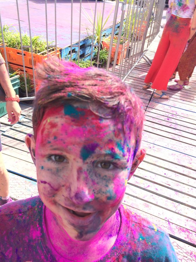 Boy covered head to toe in pink and blue Holi powder on a deck